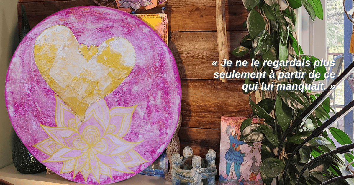 Mandala annuel de Louise posé à la verticale sur une tablette blanche, devant un mur de planches anciennes. Le mandala rose montre un lotus transparent et un grand cœur doré et blanc iridescent.